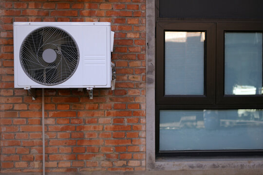 Outdoor air conditioning unit mounted on brick wall near window