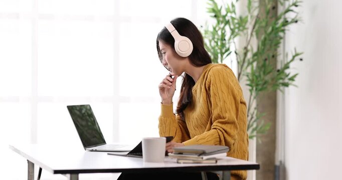 Young asian woman wearing headphones and studying online, learning new skills from home, focusing on virtual education with a laptop, happy to be collaborating remotely