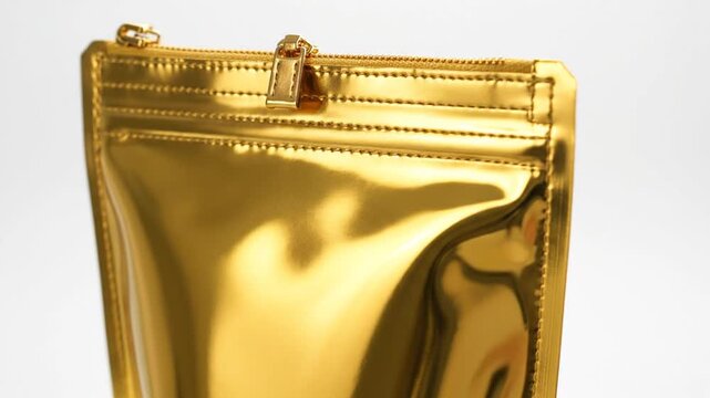 A shiny gold pouch with a zipper closure is standing upright on a white surface indoors.