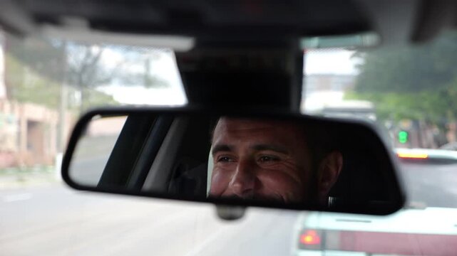 Eyes of male smiling driver reflecting in rearview mirror while riding motor auto. Young man looking concentrated to urban road during operating vehicle. Confident guy driving modern car at city