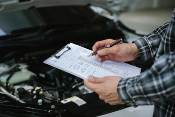 Fototapeta premium Mechanic completing a vehicle inspection checklist under an open hood, documenting maintenance findings and evaluating engine condition for professional automotive service.