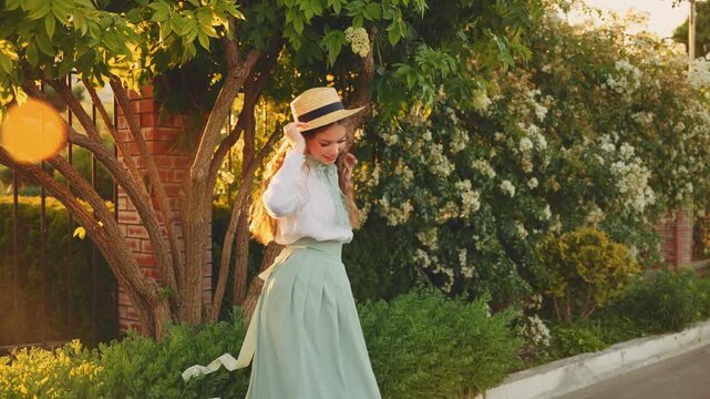 Cheerful happy joyful young woman red long loose hair fly wind throws. cute Girl spinning dancing hands raised to magic sun light flare sunset. Beauty Smiling face. summer nature reen trees. boat hat 