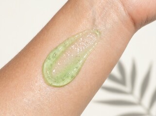 Fototapeta premium A dollop of clear green gel with small bubbles is swatched on a person's arm, with a blurred background of palm leaves.