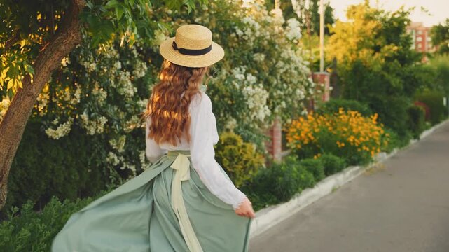 Cheerful happy joyful young woman red long loose hair fly wind throws. cute Girl spinning dancing hands raised to magic sun light flare sunset. Beauty Smiling face. summer nature reen trees. boat hat 