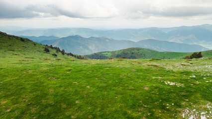 Fototapeta premium Green mountain meadow in the Pyrenees with panoramic view of rolling hills and dramatic cloudy sky in Catalonia Spain