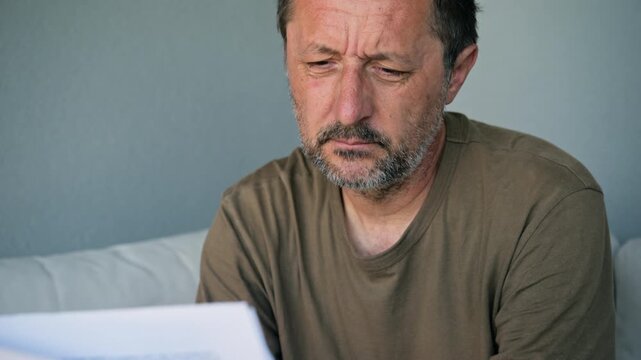 Middle-aged man reading important document looking worried and thoughtful at home, 4K