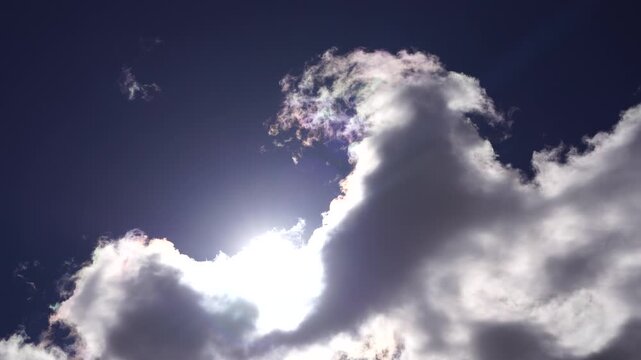 Sun shining behind dark rain clouds in blue sky. Weather and climate concept. Nature sky photography.