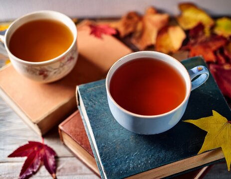 warm tea in cups with old books and colorful fall leaves creating a cozy atmosphere