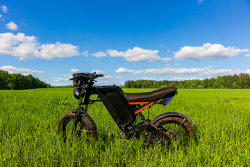 Modern electric fat bike with full suspension standing in a vibrant green meadow under a bright blue summer sky, perfect for eco-friendly off-road adventures and sustainable travel © PhotoChur