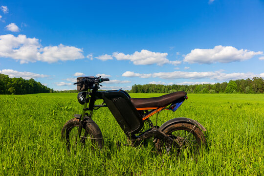 Modern electric fat bike with full suspension standing in a vibrant green meadow under a bright blue summer sky, perfect for eco-friendly off-road adventures and sustainable travel