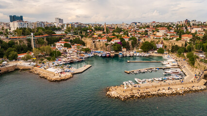 Obraz premium Wide aerial drone view of the ancient Roman harbor in Antalya old town Kaleici, showing docked boats, historic stone walls and the modern city residential skyline, Turkey
