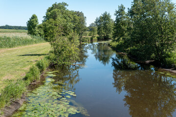 Obraz premium People walk beside a river in a green field under a clear sky during daylight hours
