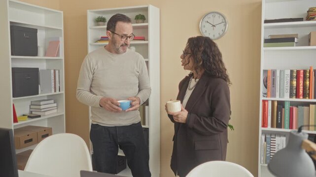 Man holding blue coffee cup points finger at woman during casual office meeting in building; serious discussion.
