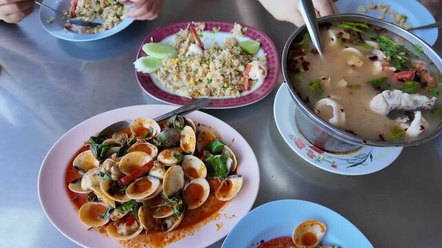 A Feast for the Senses: A vibrant spread of authentic Thai cuisine, featuring a steaming bowl of Tom Yum soup, stir-fried clams, and flavorful fried rice, promises a delightful culinary journey.