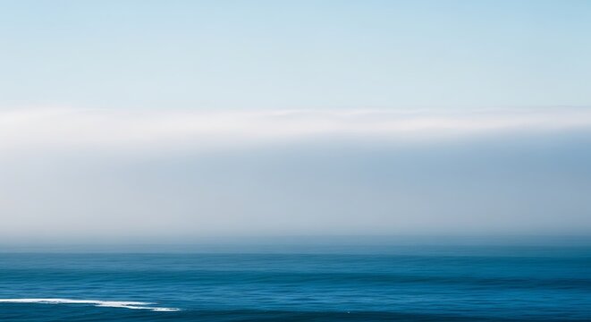 Thick white fog bank rolling over deep blue ocean waters