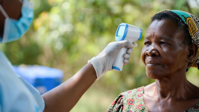 Ebola hemorrhagic fever epidemic prevention medical checkpoint outdoor field healthcare worker measuring senior woman patient temperature non contact infrared thermometer gun close up