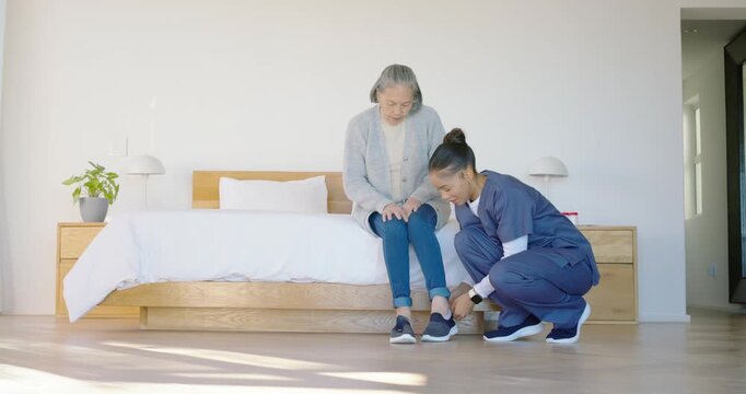 Nurse kneeling in bedroom, tying shoes for Senior Asian, placing walker, preparing to help stand