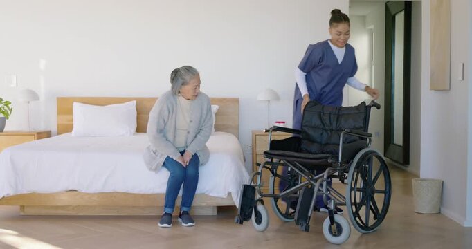 African American aide in scrubs placing wheelchair and helping Asian senior woman transfer from bed