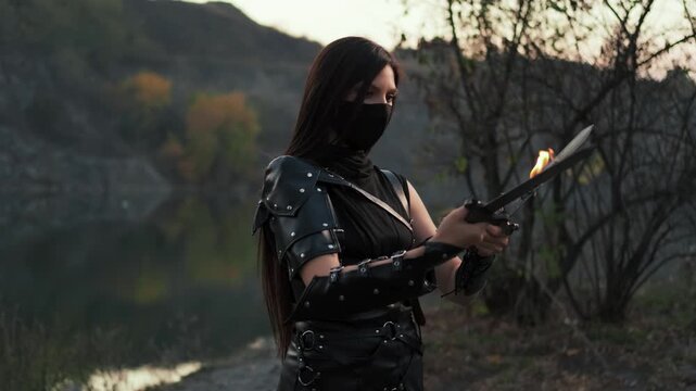 Portrait fantasy woman warrior assassin holding two burning flame fire blade daggers in hands. hiding face mask. Armed warlike girl. Black leather costume ninja soldier. sexy fashion model posing 4k 