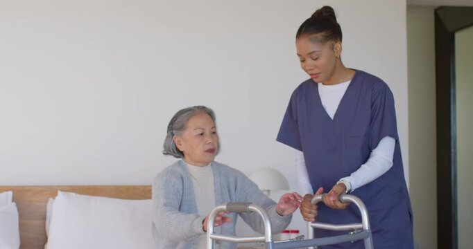 Senior Asian woman and nurse in scrubs bringing walker adjusting grips helping stand for walking