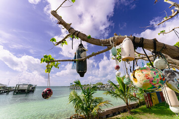 Colorful fishing buoys and floats hanging from driftwood trees along the tropical waterfront of Green Turtle Cay, Bahamas, with crystal-clear turquoise water, marina docks, and dramatic Caribbean sky. © Randy