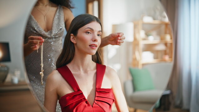 Two women proposing jewelry to friend looking mirror wearing red dress closeup.