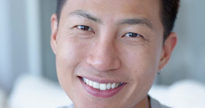 Asian mid adult man in soft-lit room reacting to cue, widening, squinting, showing hoop earring