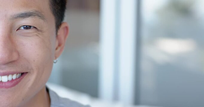 Asian man 30s smiling, shifting from neutral to broad grin near window, hoop earring, copy space
