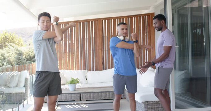 Diverse men on coach cue stretching arms on patio while right man assisting center with headphones