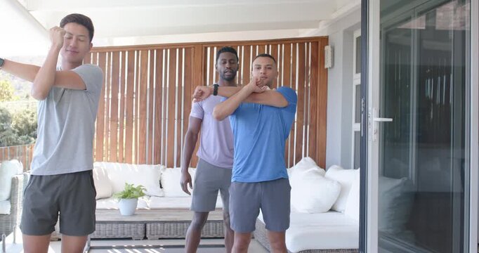 Diverse male friends following center cueing, warming up and stretching on patio with headphones
