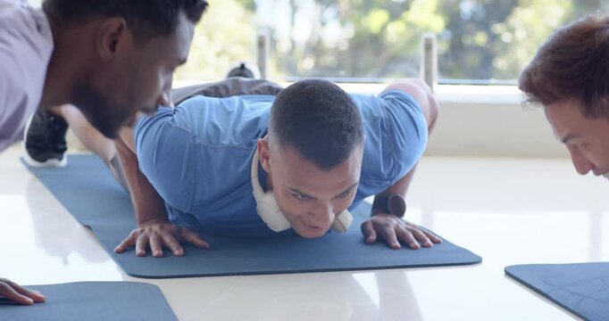 Asian man responding to high-five, supporting one hand and doing push-ups on blue mat in studio