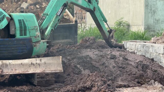 An excavator pushes soil beside a concrete boundary structure while performing leveling activity on a prepared construction site surface outdoors. Ground leveling.