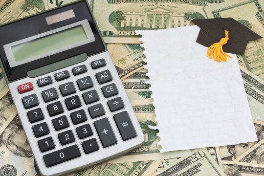 Calculator with torn paper and grad cap on twenty dollar bills for cost of education