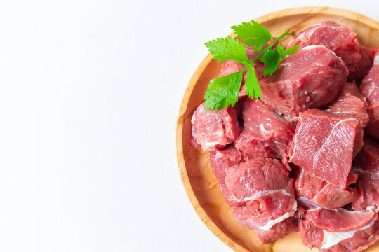 Fresh raw beef meat slices in a wooden plate on white background with copy space. Lamb red meat chopped in small cuts ready for skewers. Top view with space for your text
