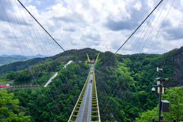 The modern pedestrian suspension bridge in the mountains background white clouds and blue sky.