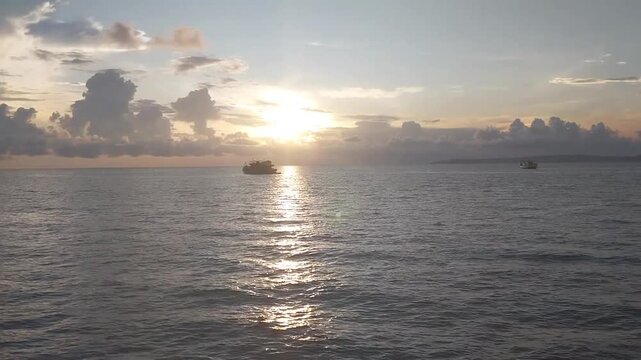 Silhouette of a cargo ship on the ocean at sunset with golden sunlight reflection.