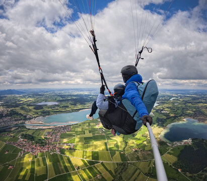Tandem paragliding pilot and passenger flying from Tegelberg over Lake Forggensee ideal for adventure travel marketing