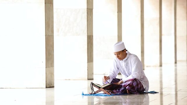 Muslim man reading the Quran inside a bright, modern mosque hallway
