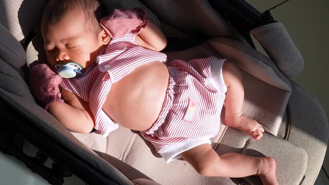 Cute newborn baby sleeping peacefully with a pacifier inside a stroller under warm sunlight