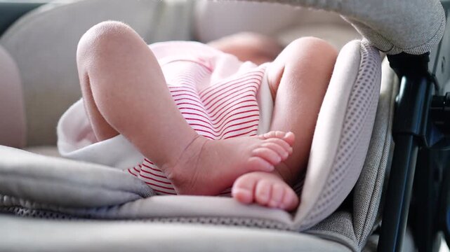 Close up view of cute newborn baby legs and feet resting comfortably inside a stroller car seat