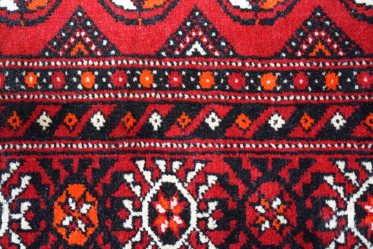 Traditional red Turkmen carpet with Tekke guls pattern close up, handmade wool rug texture detail macro of oriental tribal ornaments from Turkmenistan 