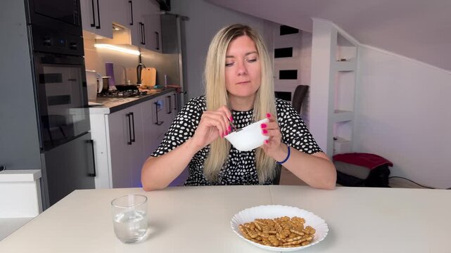 Woman Eating Simple Dinner In Kitchen, Black Plate With Protein And Rice, Fork And Glass Of Water, Blonde