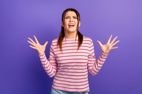 Frustrated young woman shouting and gesturing with hands, expressing anger, stress and exasperation while standing against a vibrant purple background