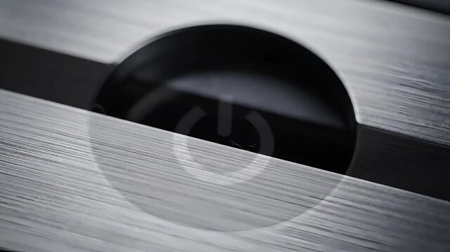 Close up of a black power button with a white symbol on a metallic surface.