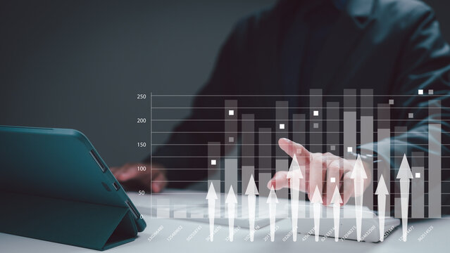 Business person touches digital bar chart overlaying tablet screen analyze financial growth trends during office work session in dim environment, highlighting data visualization strategic investment.