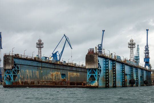 Large rusty floating dry dock with industrial cranes at shipyard harbor, maritime heavy industry and vessel maintenance