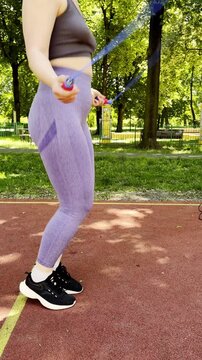 Young Woman Active Outdoor Workout. Active Young Woman Engaged In Outdoor Jump Rope Exercise Near Trees