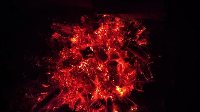 Close up of glowing charcoal embers burning with red and orange tones at night. Soft heat and shimmering texture create magical atmosphere. Warm abstract scene symbolizing warmth and quiet at nature