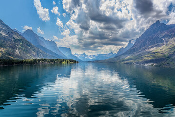Turquoise Saint Mary Lake surrounded by steep forested mountain slopes and weathered tree stumps under a bright blue Montana sky in Glacier National Park © Martina