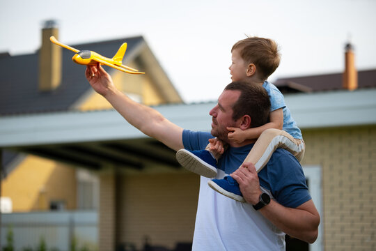 Playing with toy plane, sitting on father's shoulders. Happy family father and son playing and laughing outside. Father's day. Happy childhood and parenthood. Kids adventure, memories, imagination,
